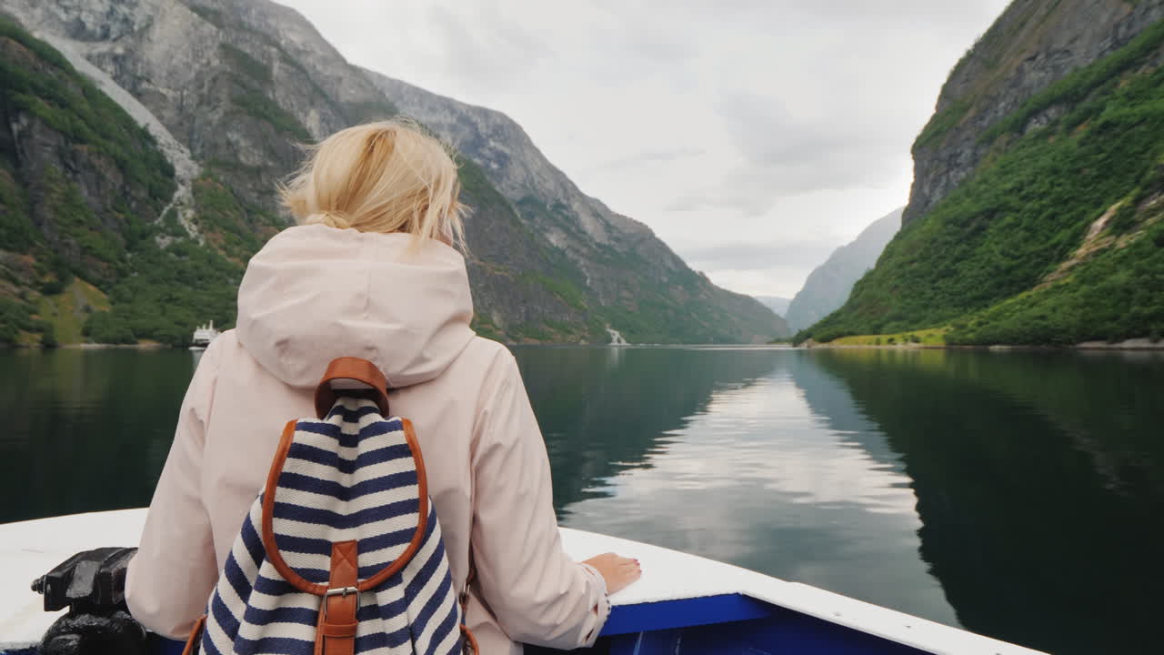 한 여성이 노르웨이 피요르드에서 쌍안경 순항을 통해 바라보는 배의 뱃머리에 서 있다