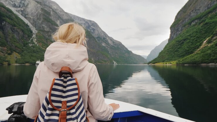 Eine Frau steht am Bug des Schiffes und blickt durch ein Fernglas Kreuzfahrt auf den Fjorden Norwegens