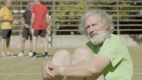 jugador de fútbol senior pensativo sentado en el campo y mirando a la cámara