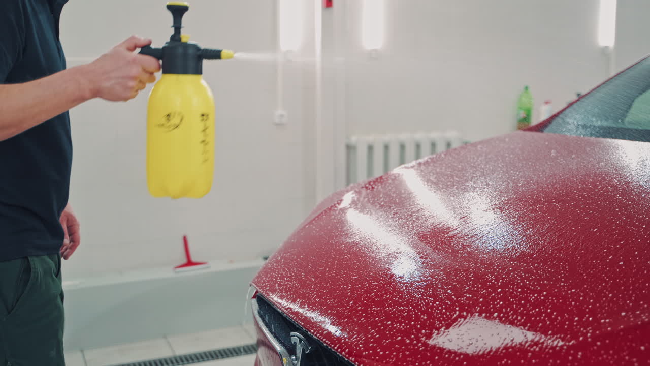 Man cleaning red Tesla. Worker wash cleaning brush on car at service station