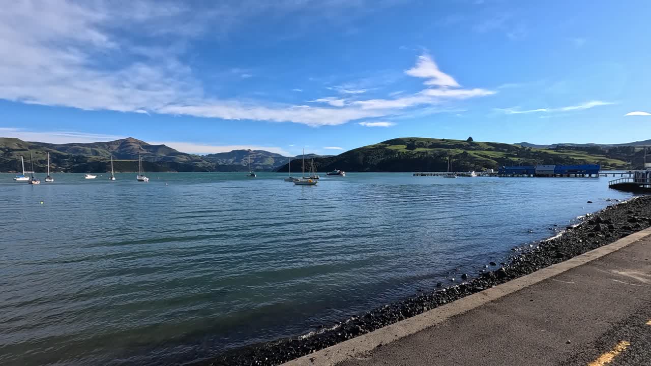 A serene drive along Akaroa's waterfront, showcasing calm waters, boats, and a picturesque sunrise with vibrant skies