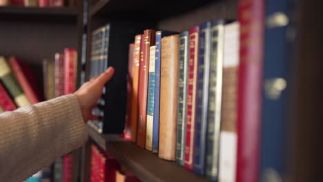 Hand-sweeps-across-blue-covered-almanacs-and-stops-to-pull-book-off-wooden-shelf