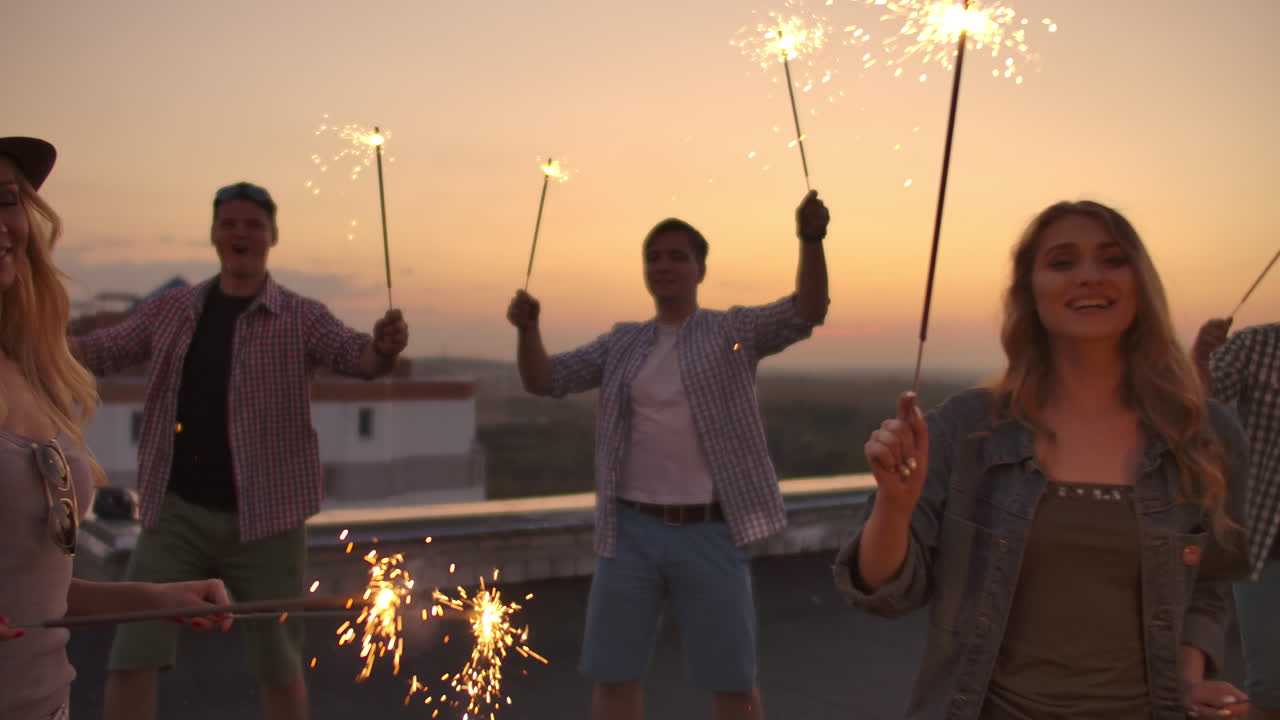 Young people on the roof move a dance on a summer evening with big bengal light. It's a pleasure sunset before night.