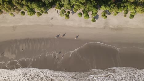 People-on-three-horses-slowly-ride-along-beautiful-Manuel-Antonio-beach-at-sunset-with-tropical-nature-bordering-at-the-ocean