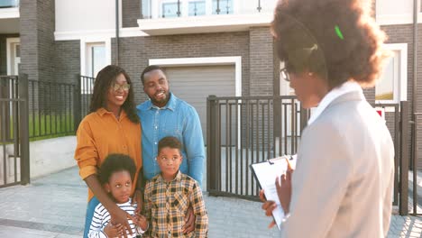 feliz familia afroamericana con dos niños pequeños comprando una casa en los suburbios y hablando con una agente inmobiliaria al aire libre