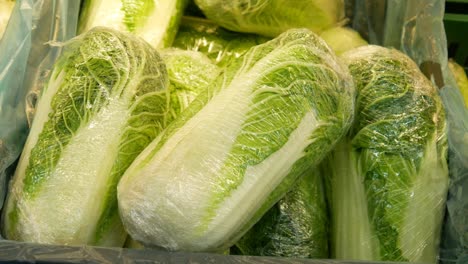 close-up of a many packaged chinese cabbages in the market and a male hand takes one