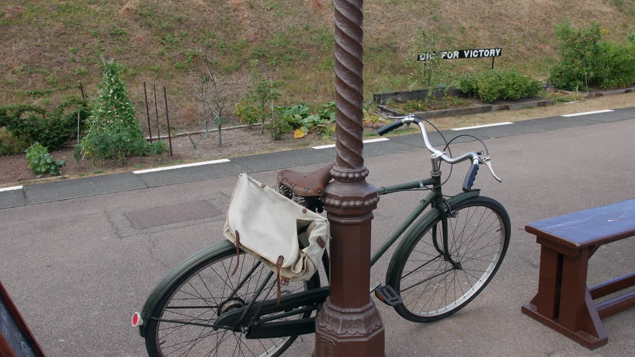 una bicicleta antigua apoyada en un poste en una estación de tren durante la segunda guerra mundial con una excavación británica para el signo de la victoria
