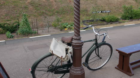 a vintage bicycle leaning on a post at a train station during world war two with a british dig for victory sign