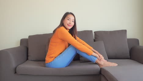 Smiling-woman-relaxes-on-sofa-and-looks-into-camera