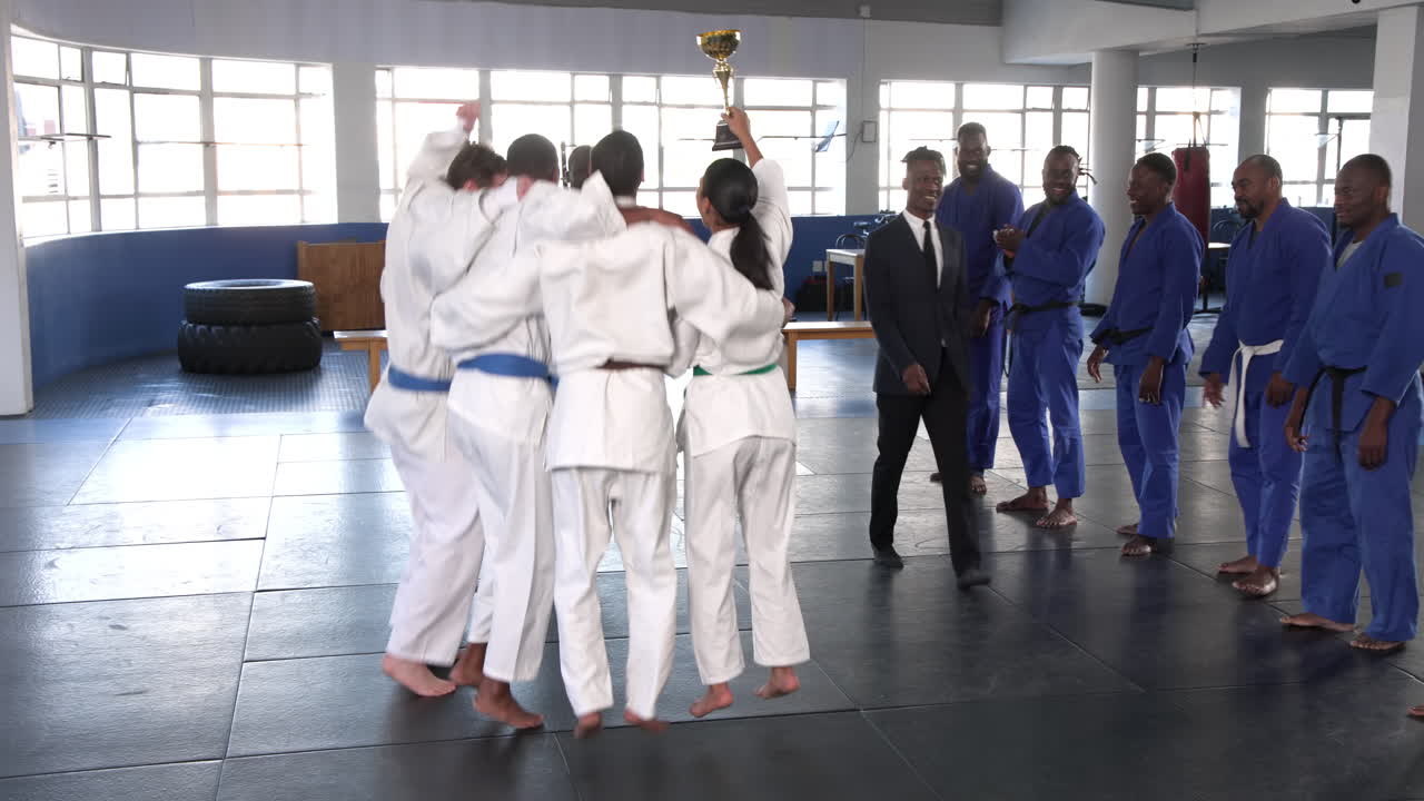 Celebrating victory, judo team in white uniforms holding trophy in dojo