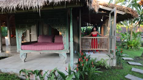 tan asian girl leaning on balcony window in a traditional bali villa during sunny morning