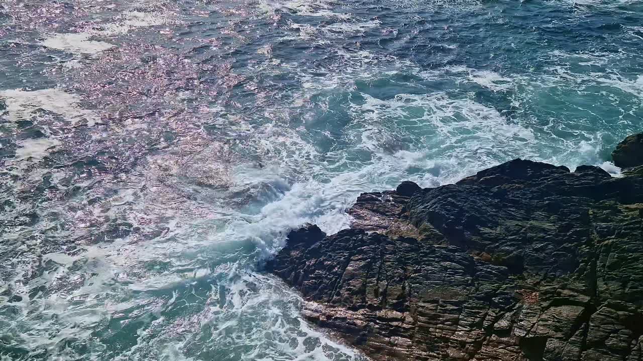 Overhead close-up of waves crashing on dark coastal rocks in Brittany, France.
