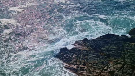 overhead close-up of waves crashing on dark coastal rocks in brittany, france.