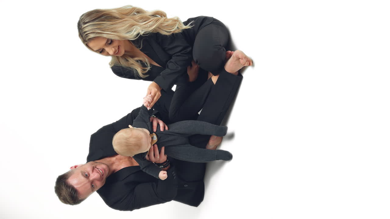 Parents of an infant baby sit on the floor in studio. Smiling couple playing with their beloved son. Vertical screen.