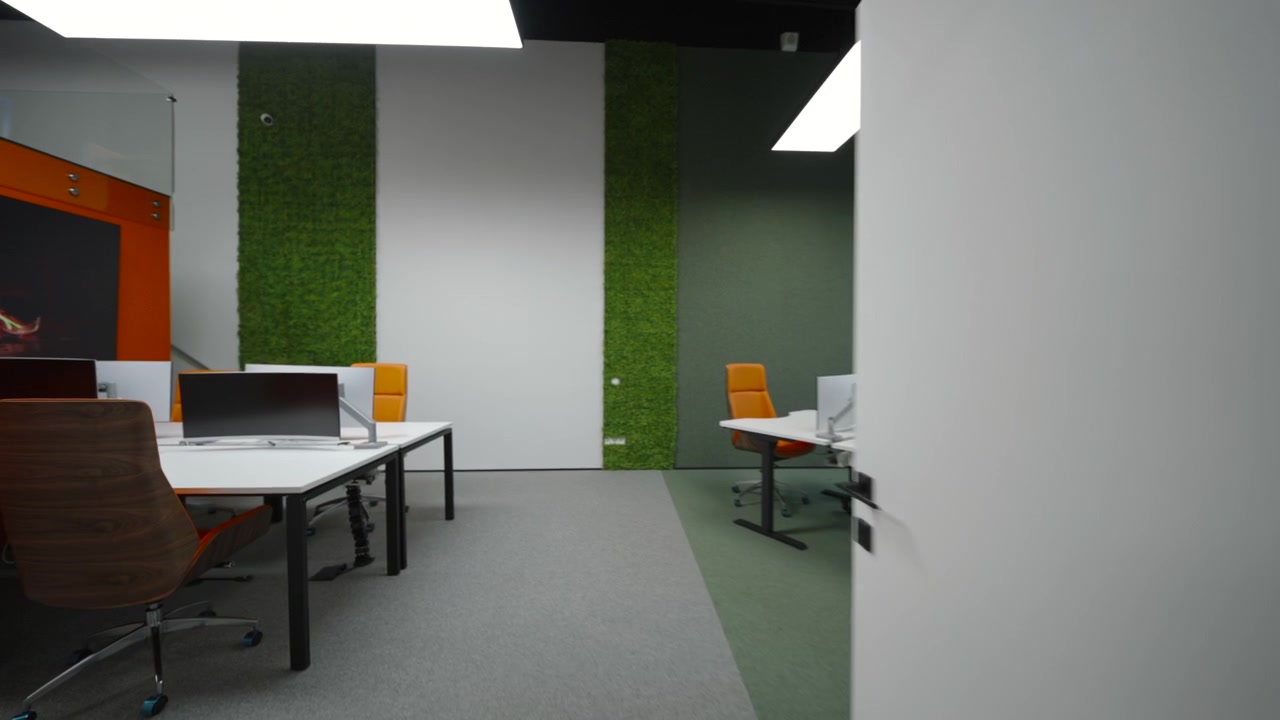 Contemporary indoor workspace or lobby with a desk in the foreground, stepped seating on the right, an open doorway, staircase, indoor plants, and soft warm