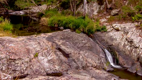 timelapse of pond flowing into small waterfall flowing over rocks surrounded by grass