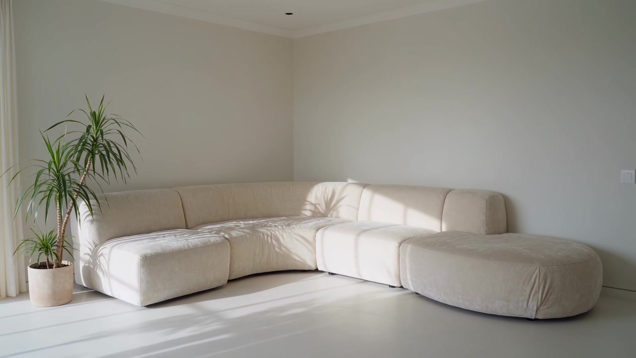 Luce solare che si sposta, scivolando da tende trasparenti su un divano beige in casa, con l'ombra di una pianta in movimento.
