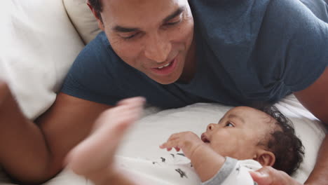 cerca de un padre afroamericano del milenio acostado en la cama jugando con su hijo recién nacido