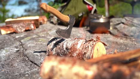 hiking axe inserte in a birch log with bonfire and flames in blurred out foreground - handheld slow motion hiking clip from forest