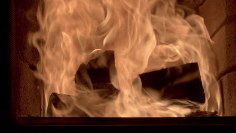 Closeup-truck-shot-of-some-large-logs-burning-inside-a-brick-fireplace,-high-fast-flames