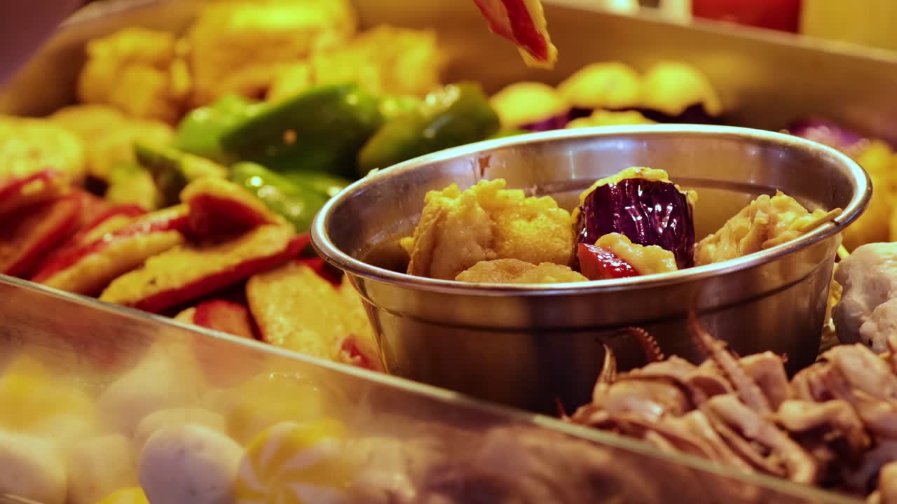 A vibrant assortment of food items with a metal bowl and tongs in focus.