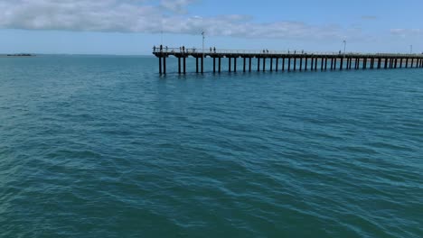 Drone-flying-over-blue-waters-and-around-Urangan-wooden-pier-at-Fraser-Island,-Queensland-in-Australia