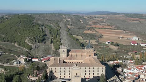 Vuelo-Inverso-Visualizando-El-Impresionante-Monasterio-De-Ucles-Fundado-En-El-Siglo-XII-Y-Ampliado-En-El-Siglo-XVI-XVII,-Aparece-Su-Maravilloso-Entorno-Y-El-Pueblo-De-Ucles