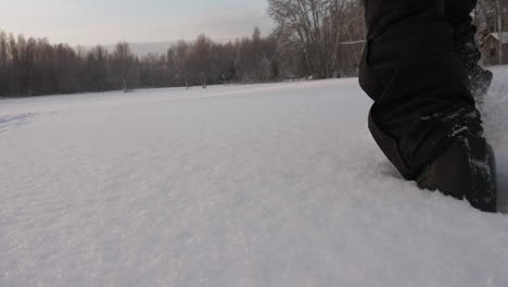 Winter-boots-walking-into-deep-snow-in-a-large-field-surrounded-by-forest