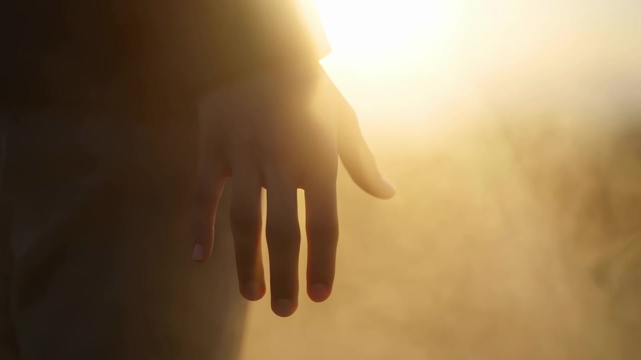 Un paio di mani che si protendono in una scena esterna illuminata dal sole, evocando un'atmosfera di speranza e serenità. La prospettiva ravvicinata evidenzia i materiali della pelle e dell'aria, con colori gialli e marroni