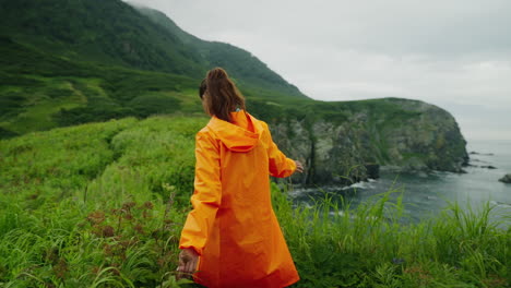Woman in Orange Rain Jacket Hiking in Mountains by the Sea