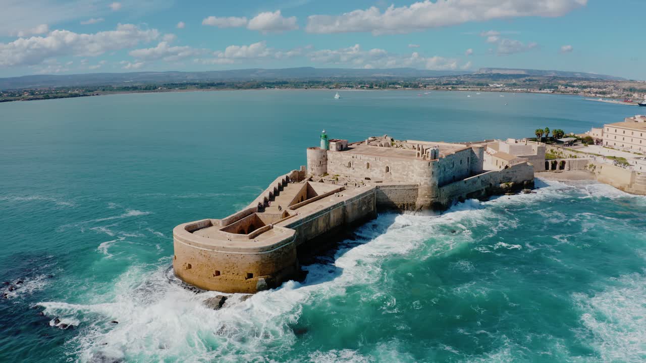 Aerial view of Castello Maniace in Ortigia island, Syracuse. Medieval castle surrounded by Mediterranean sea in Sicily. Big waves crashing into the fortress walls.