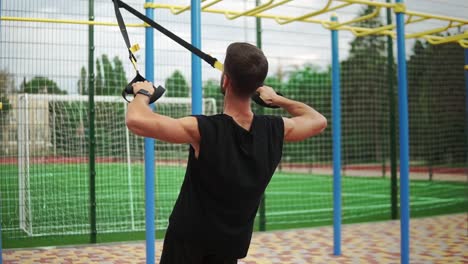 an athletic man doing exercise using rubber belt to force strenth of workout on chest muscles and biceps