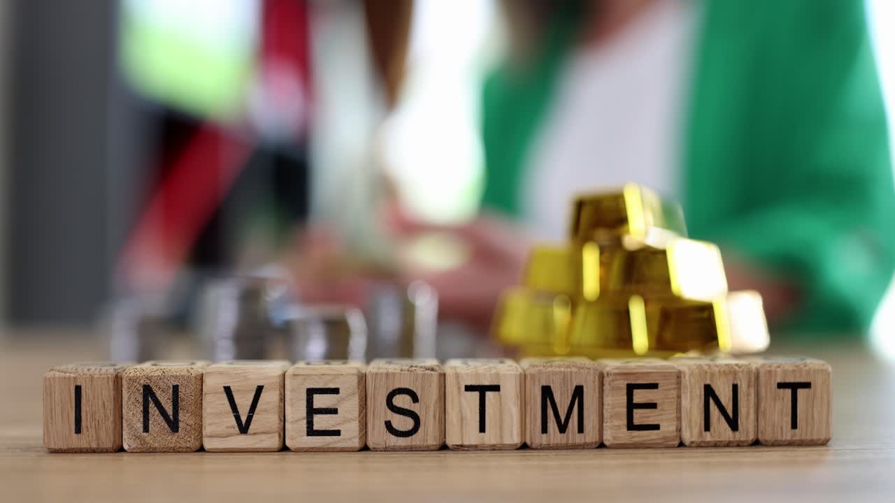 Wooden blocks spelling 'INVESTMENT' with gold bars and coins, symbolizing financial growth