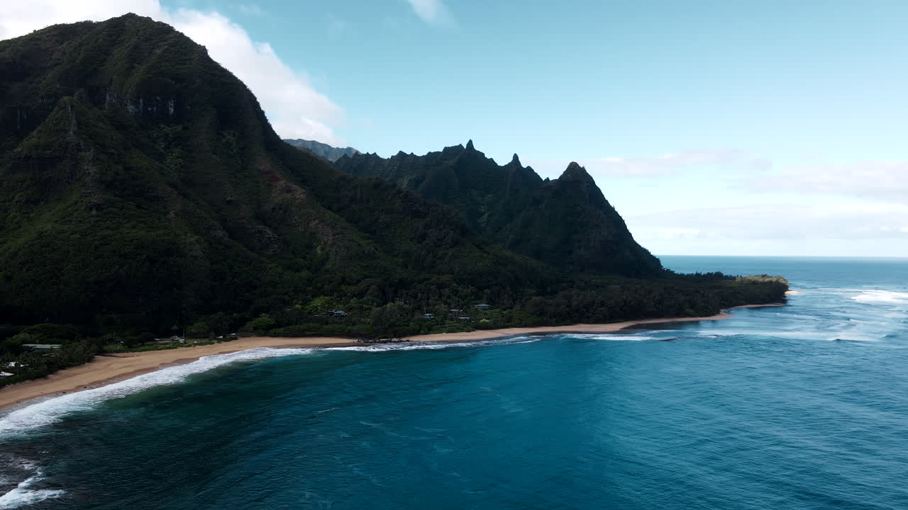 Dark Emerald Mountains Rise over Clear Ocean Waters and Beach
