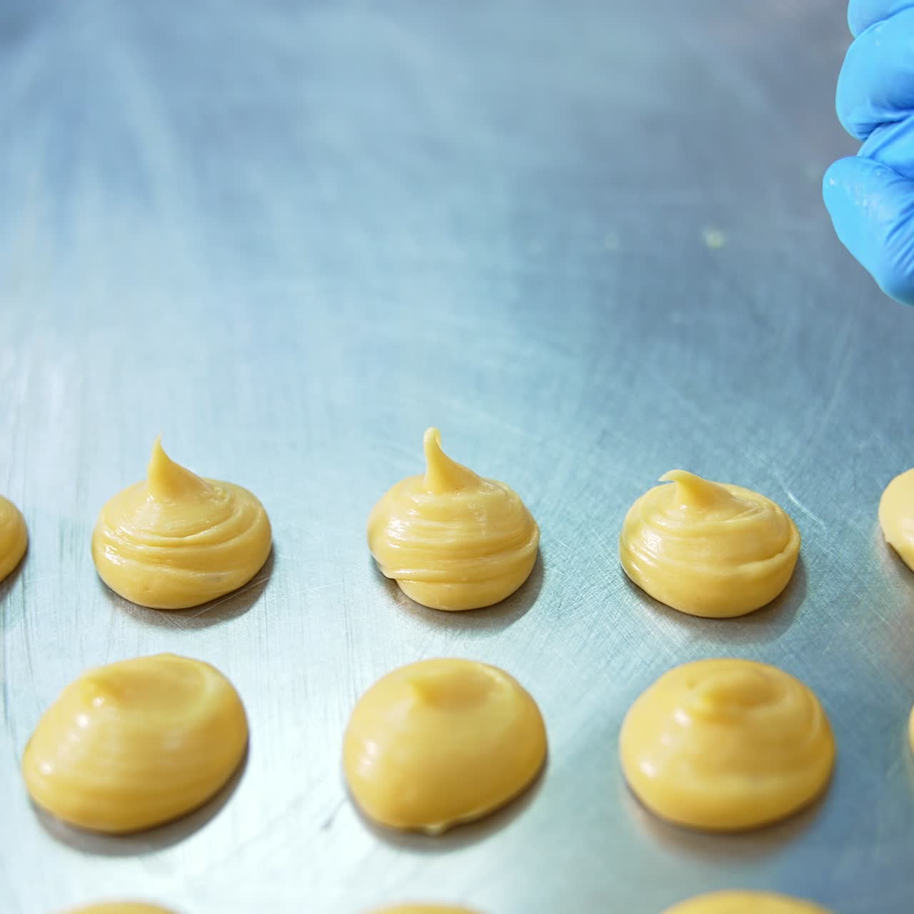 Yellow liquid pastry dough being squeezed on the baking sheet. Close up. Pastry production at confectionery factory