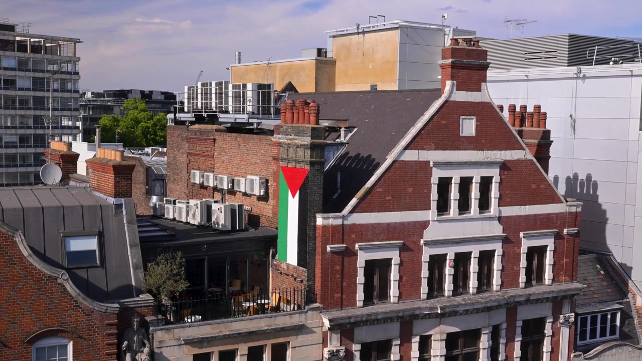 Bandiera palestinese che pende da un alto camino in mattoni su un edificio in mattoni rossi a Holborn, incorniciata dai tetti circostanti nella morbida luce del pomeriggio.