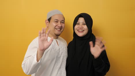 카메라를 바라보는 무슬림 부부의 초상화 미소 짓고 손을 흔들며 인사 또는 작별 인사 몸짓