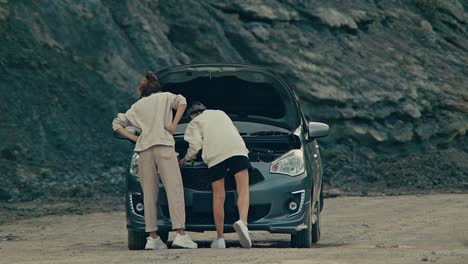 two women inspecting a broken down car in a desolate area