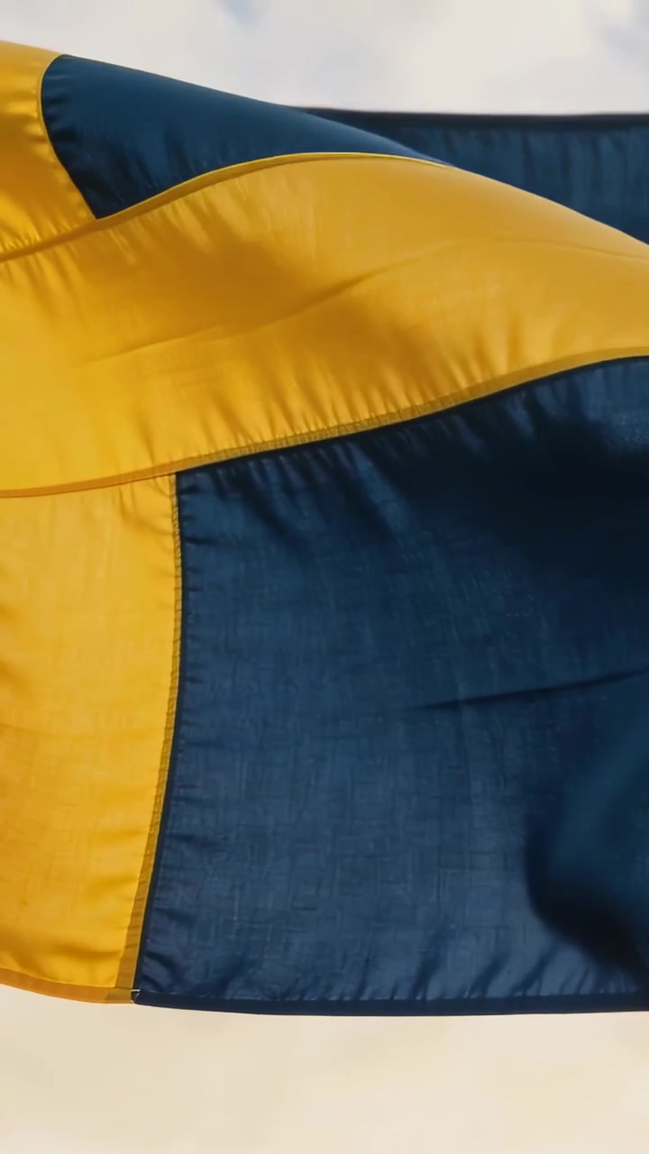 Vídeo vertical: Bandeira nórdica em cruz esvoaçando com a brisa contra céu pálido, mostrando as costuras