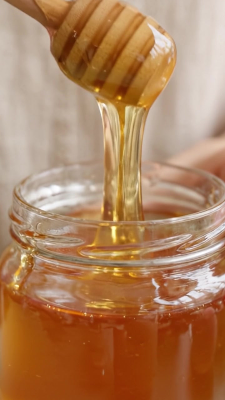 Una vista de cerca de miel siendo removida en un frasco con un cucharón de madera, mostrando la rica textura dorada y la viscosidad del dulce producto natural