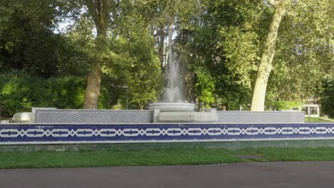 Fountain-with-water-flow-along-green-garden-under-sunlight-static-shot-panoramic