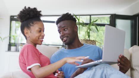 video of happy african american couple sitting on sofa and using laptop