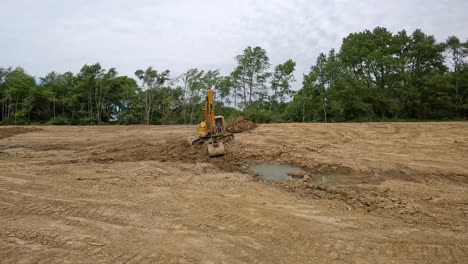 hydraulic excavator digging dirt from bottom of pond and moving it to top of side wall of pond at a land development site