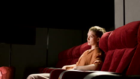vista lateral de una mujer rubia sentada en el cine y viendo una película