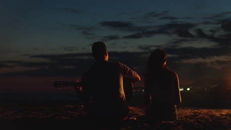 pareja tocando la guitarra en la playa por la noche