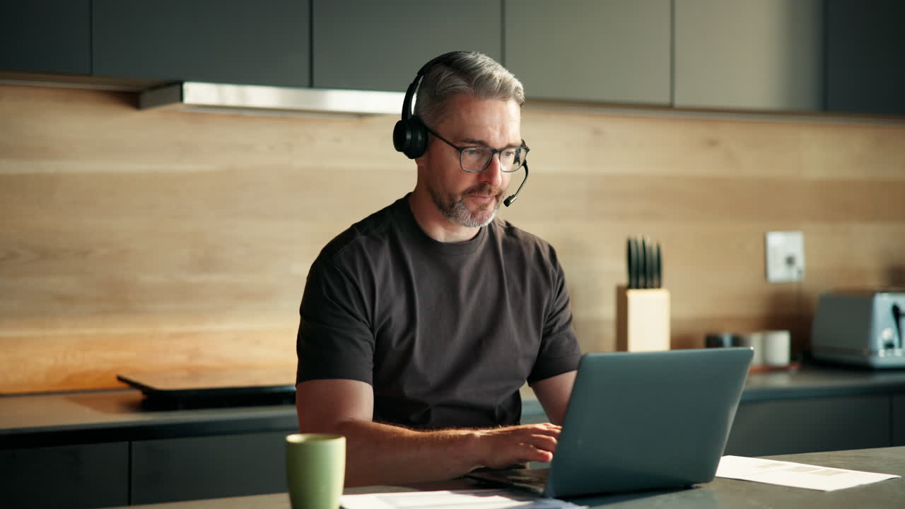 Mand med headset arbejder på bærbar computer i moderne køkken