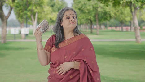 Confident-Indian-old-woman-using-money-as-fan-in-park