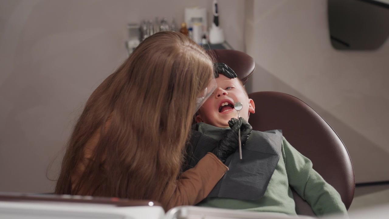 Close up of young boy receiving dental care from orthodontist in clinic. woman wearing protective gear including gloves and face shield examines child mouth with specialized instruments