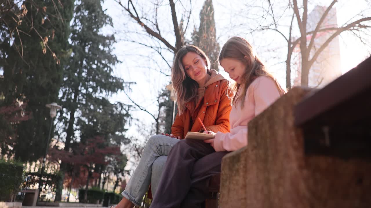 Mother and daughter writing in a notebook in the park