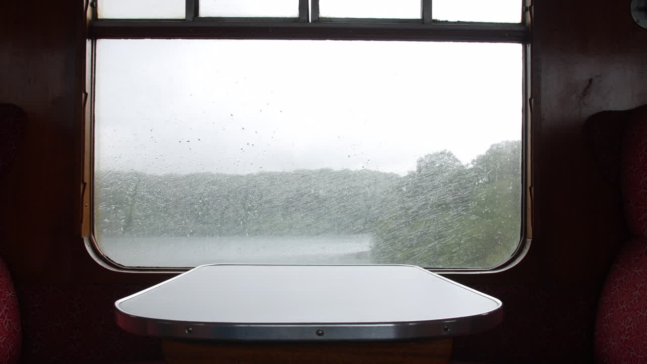 호수와 나무를 지나 철로를 따라 이동하는 빗속의 기차 창